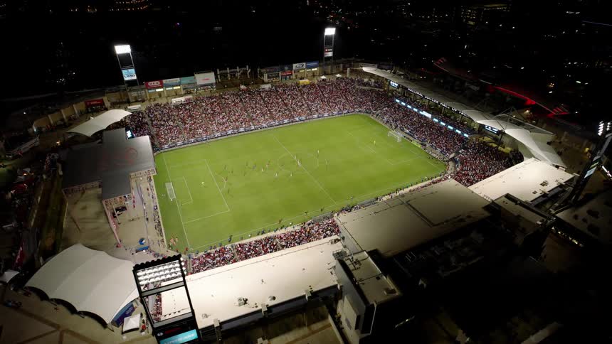 Soccer fans fill the stadium at a soccer game in the city at night