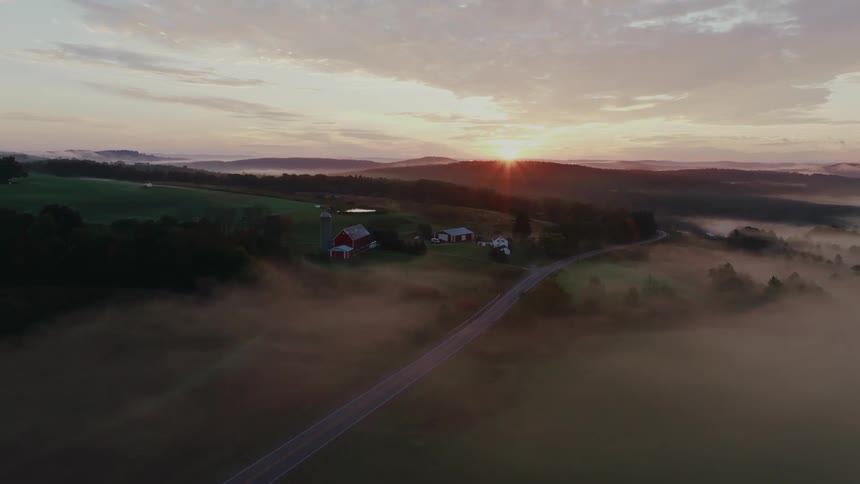 Aerial view of a green field with a foggy highway and sunrise on the horizon