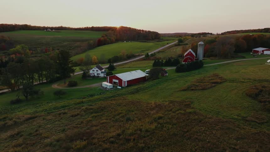 A sprawling farm nestled in a valley with rolling hills a dirt road leading to a red barn and silo and a farmhouse surrounded by lush green fields