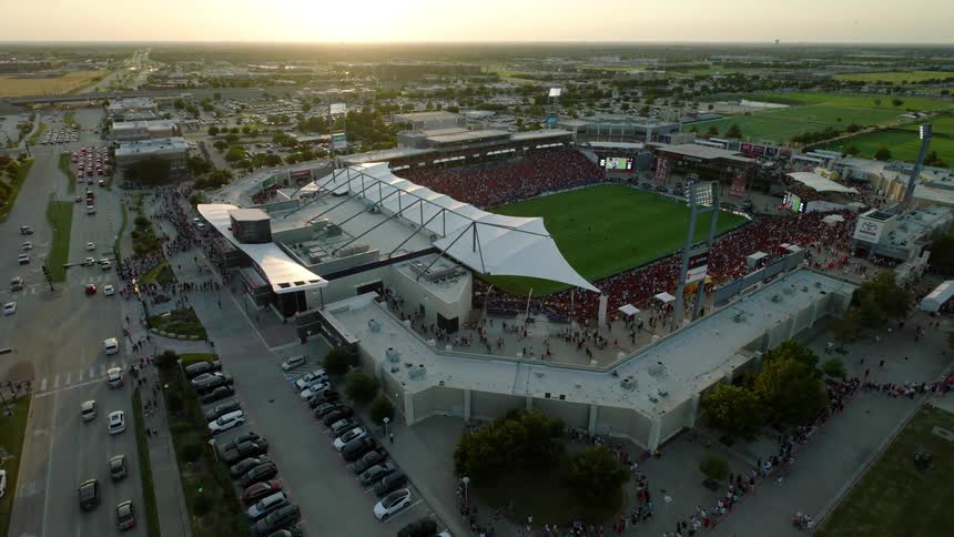 Aerial view of a packed stadium at dusk surrounded by parking lots and busy streets