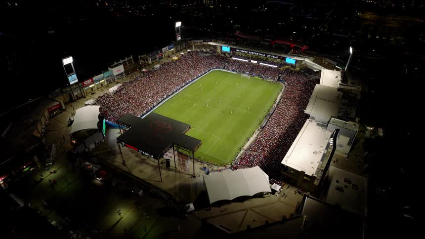 Soccer fans sit in a stadium at night watching a soccer game