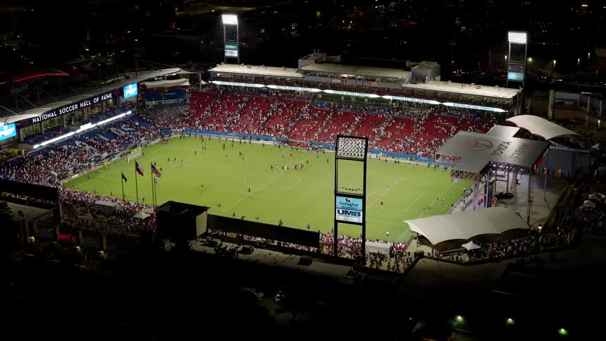 A soccer game happening at night with a packed stadium lit up and players competing on the field