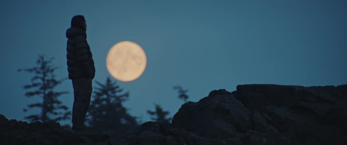 A man standing on a mountain in front of a full moon
