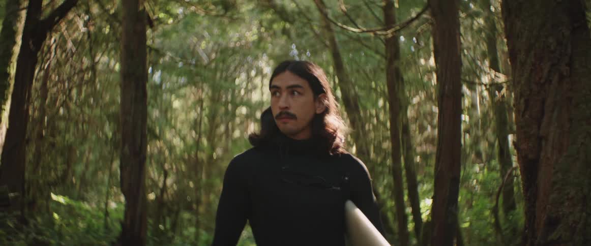 A man carries his surfboard through the forest on a sunny morning