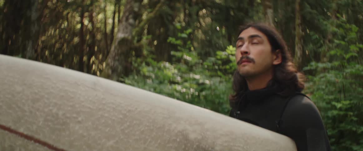 A man carries his surfboard in the forest