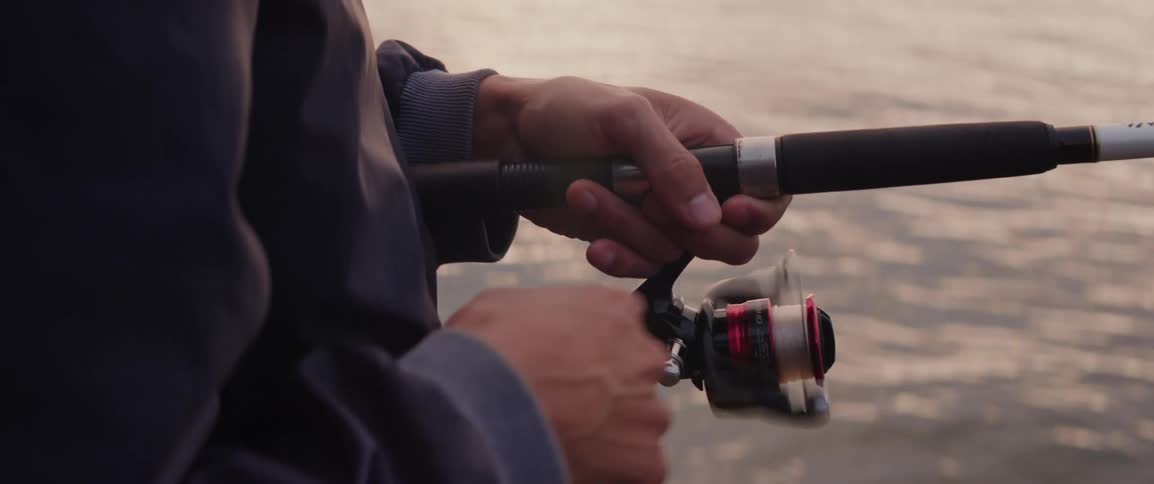 The hand of a person who is fishing on the ocean spins the reel to pull in their catch