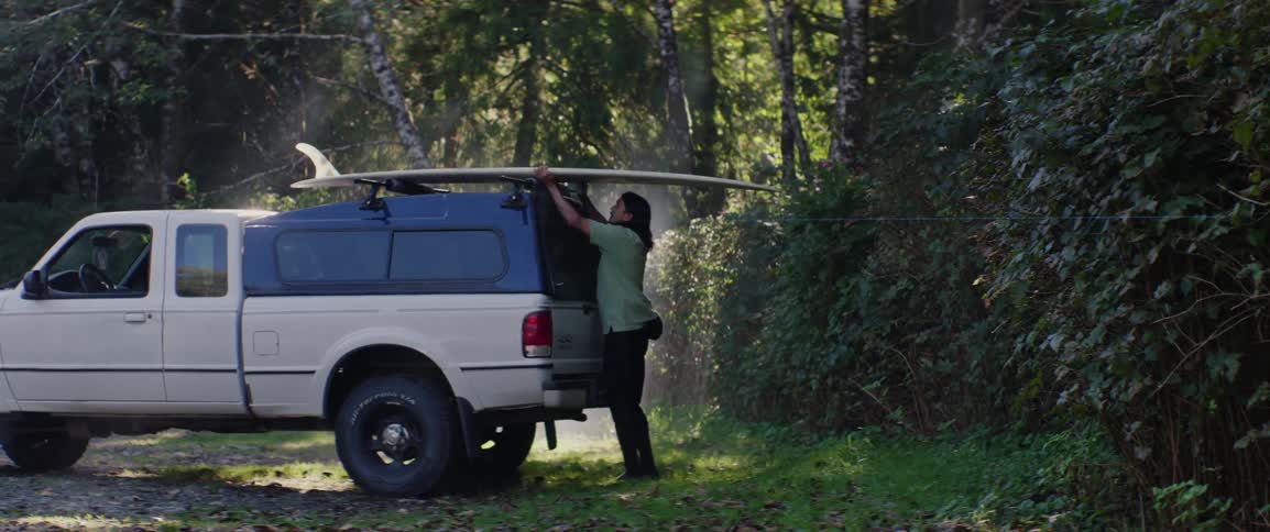 A man walks to the back of his truck and removes a surfboard
