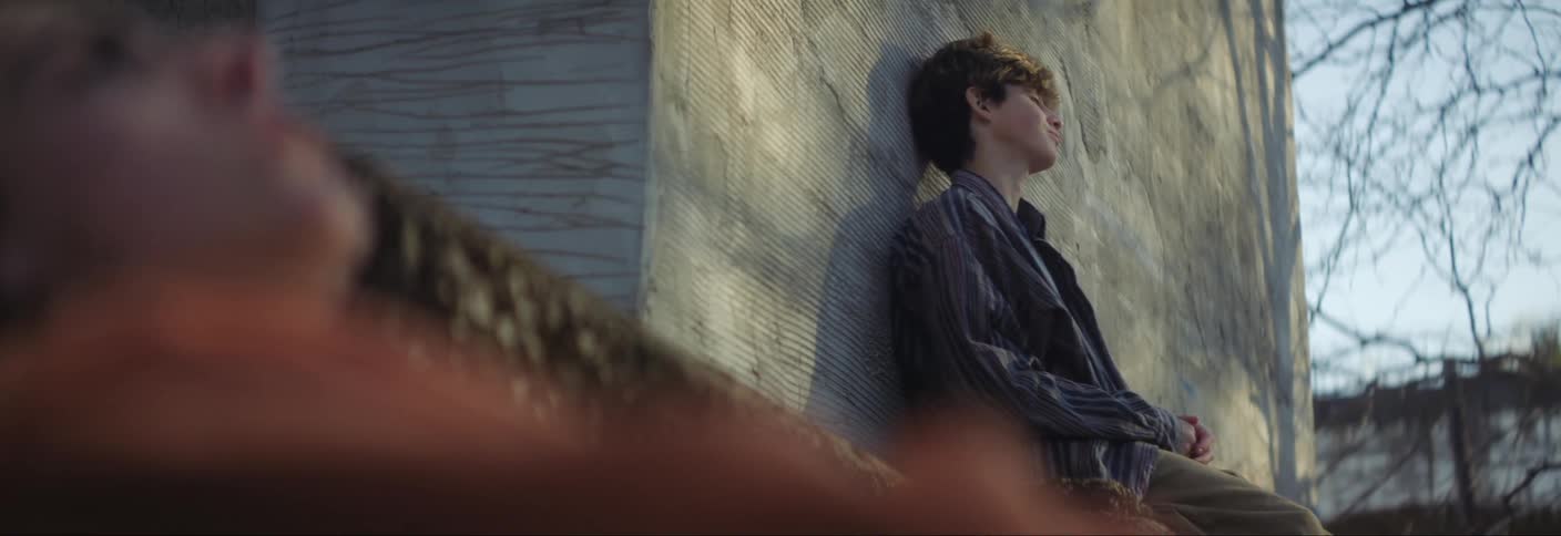 A boy sits on the ground reclined on a wall outdoors
