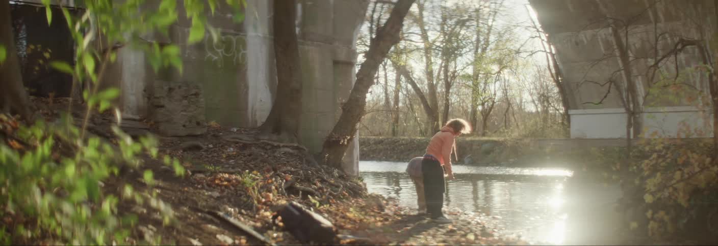 Brothers throw rocks into the river near a bridge arch on a sunny autumn day