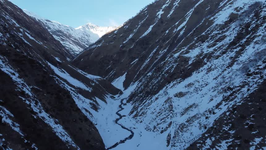 River winds through the narrow shadowed valley between mountains on a winter day