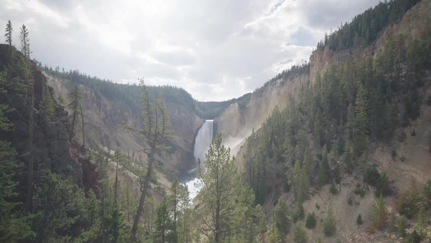 A waterfall splashes in the distance in a canyon lined with trees