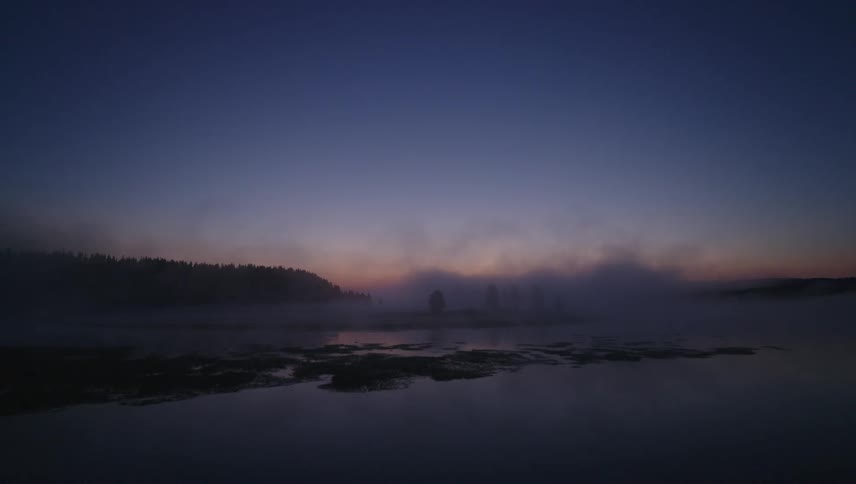 A misty lake at twilight with trees silhouetted in the distance
