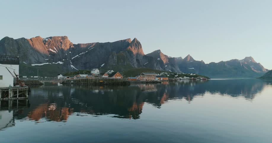 A picturesque coastal village nestled between mountain peaks with wooden houses reflecting on the calm water