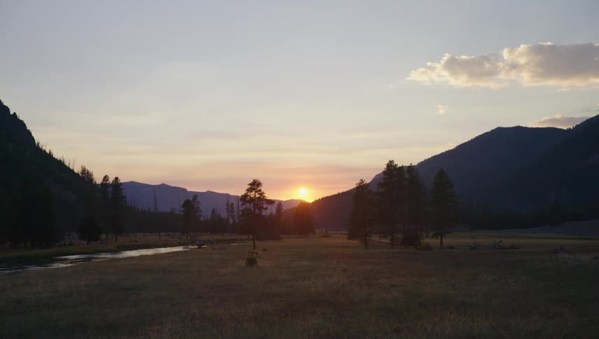 A sunset over a valley with mountains in the background a river flowing through the valley and a few trees scattered across the landscape
