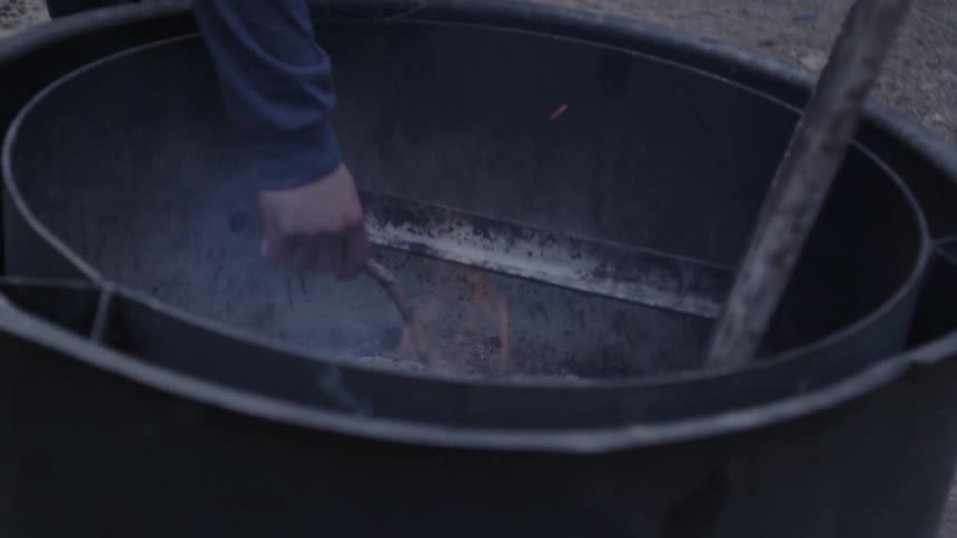 A man tends a fire in a fire pit