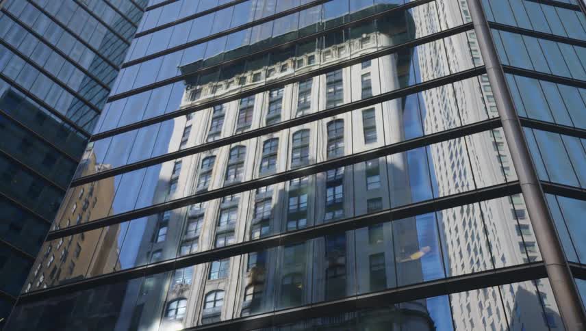 A modern skyscraper with reflective glass windows reflecting the facade of an older more ornate building