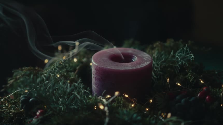 An unlit red candle with smoke coming out of the middle of it and below there are some green decorations