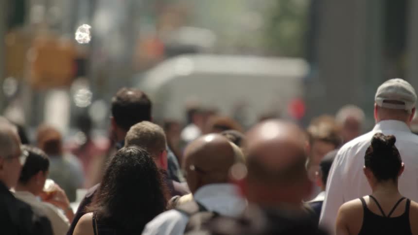 A large crowd of men and women make their way down a city street