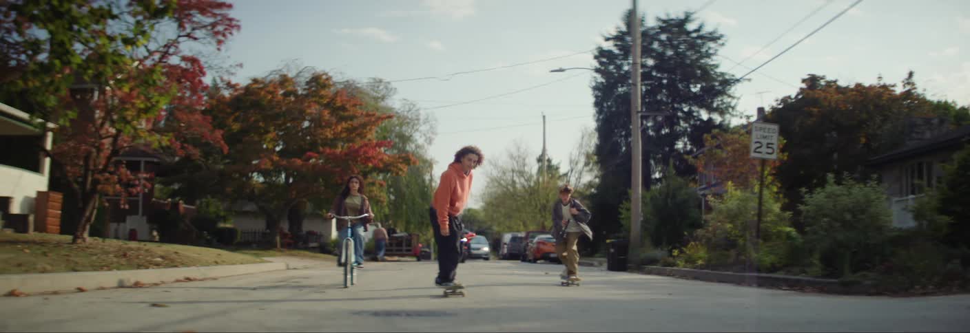 A group of children riding skateboards and bicycles on a neighborhood street