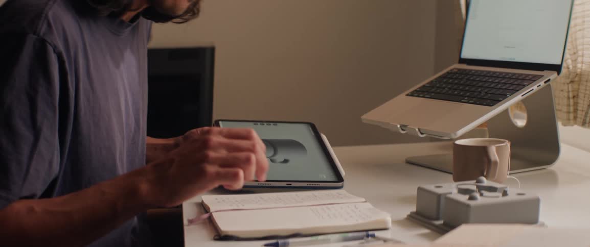 Person in a home office examines a design on a tablet and makes notes