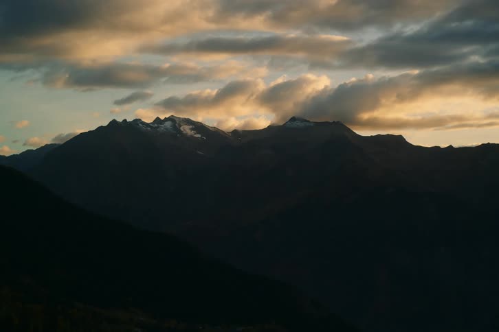 Sunset over a mountain range where the clouds are ablaze with color casting long shadows across the rugged peaks