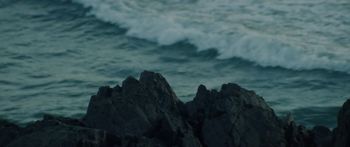 Ocean waves break behind dark jagged rocks