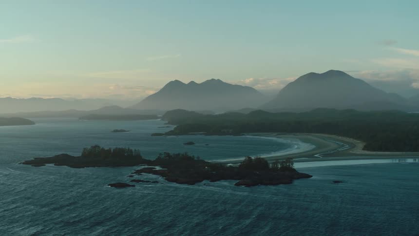 A serene coastal landscape where a beach meets the ocean framed by lush green islands and majestic mountains in the distance