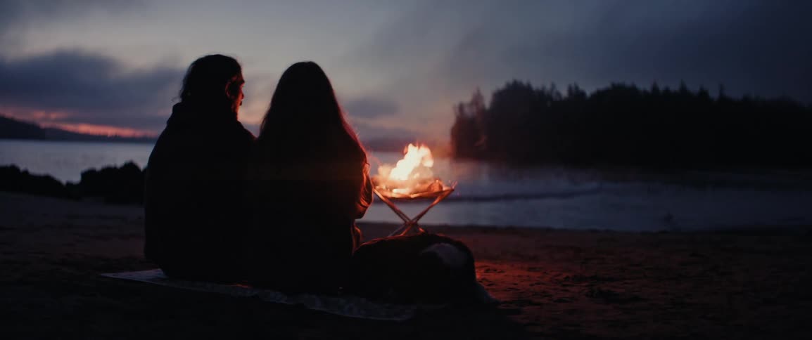 A couple sit by the fire near the ocean