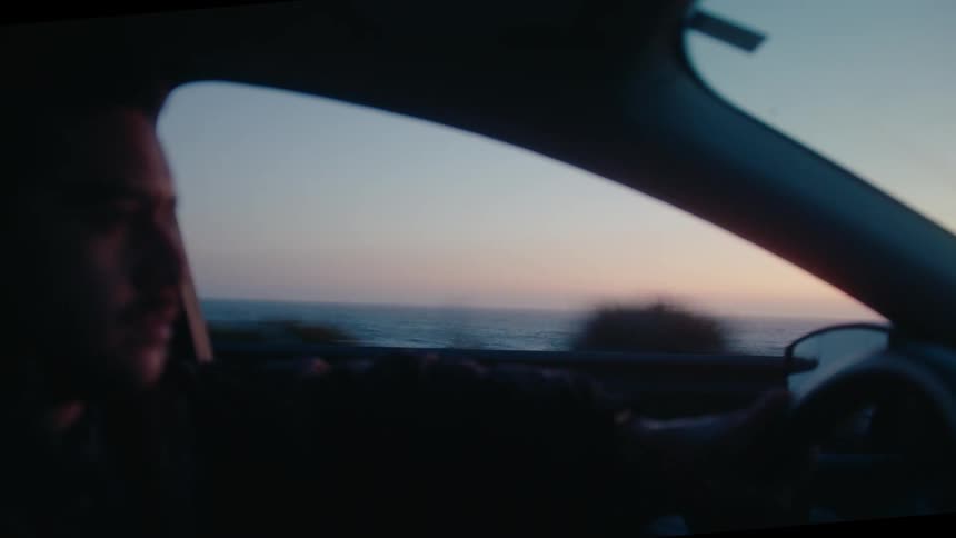 Man driving a vehicle in a seaside setting at sunrise