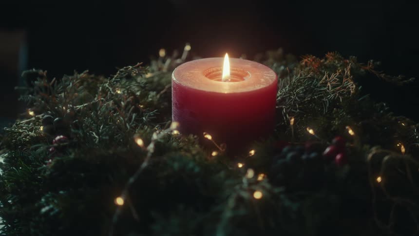 Lit candle sits surrounded by christmas lights and conifer twigs