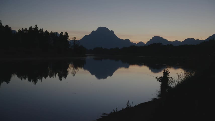 A man is fishing in the lake at sunset