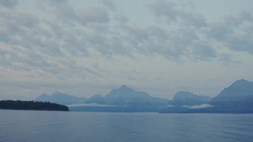 Fog obscures the mountains and forest on the coast under a cloudy sky