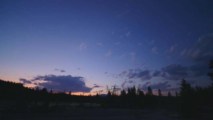 A landscape of a region with the silhouette of a forest at sunset with the sky turning dark blue
