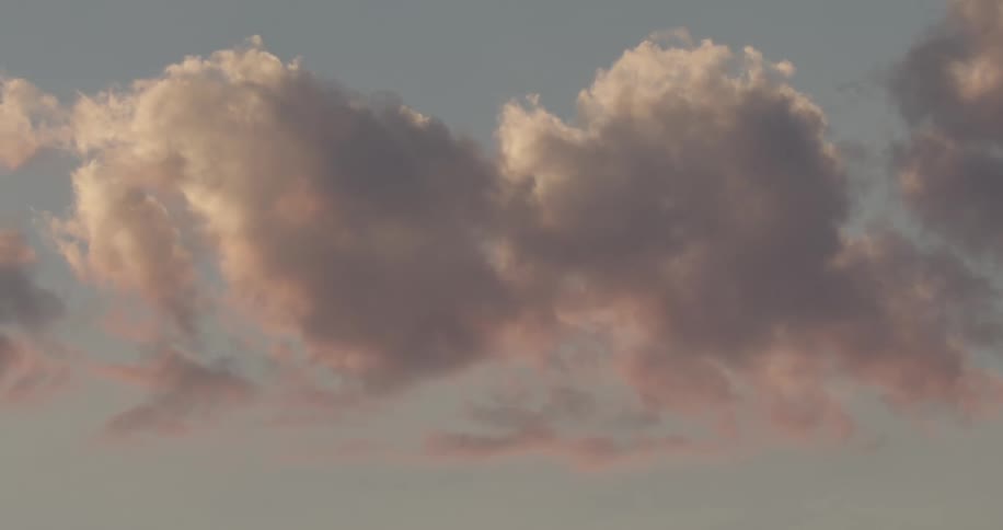 Soft fluffy clouds drift across a pastel sky at sunset