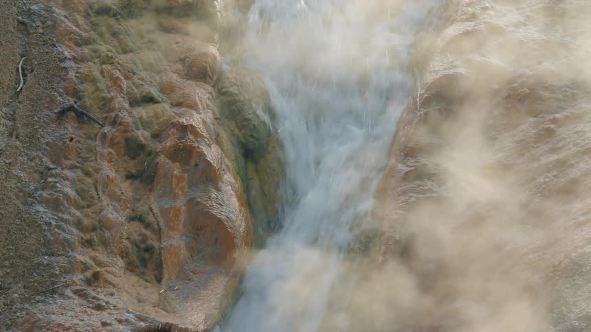 Vapor rises from a narrow waterfall during the daytime