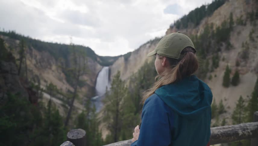 A young woman stands on an overlook and takes a photo of yellowstone falls