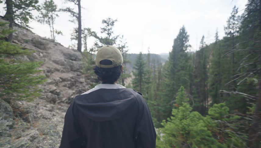 Man walking on a mountain trail overlooking the forested valley below