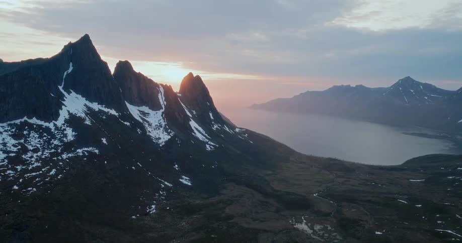 Snow on mountains along the coast as sunlight shines through the clouds in the distance