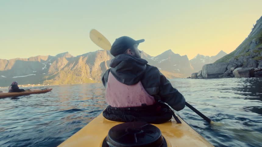 A person is kayaking on a calm body of water surrounded by towering rugged mountains under a clear sky