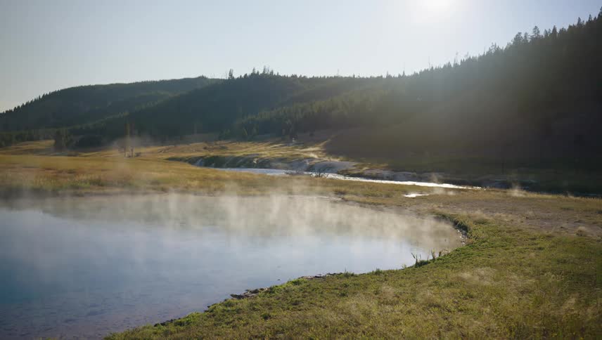 A geothermal hot spring nestled amidst a picturesque landscape with a river winding through the valley and a backdrop of lush green hills