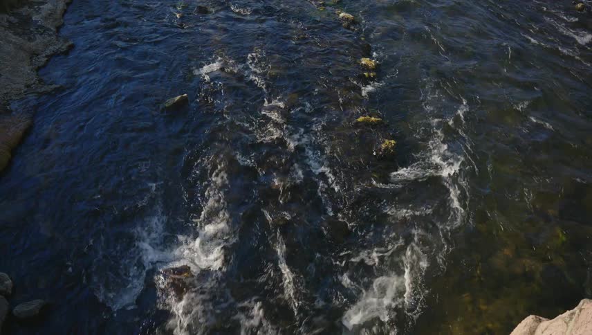 A river flows swiftly over a rocky bed creating a turbulent pattern of whitewater and dark depths
