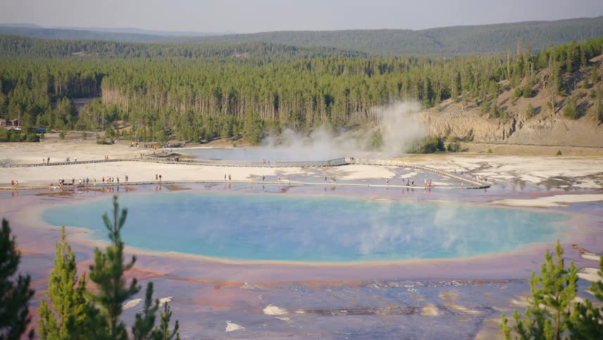 A pool of blue water from a geyser shooting white steam upwards