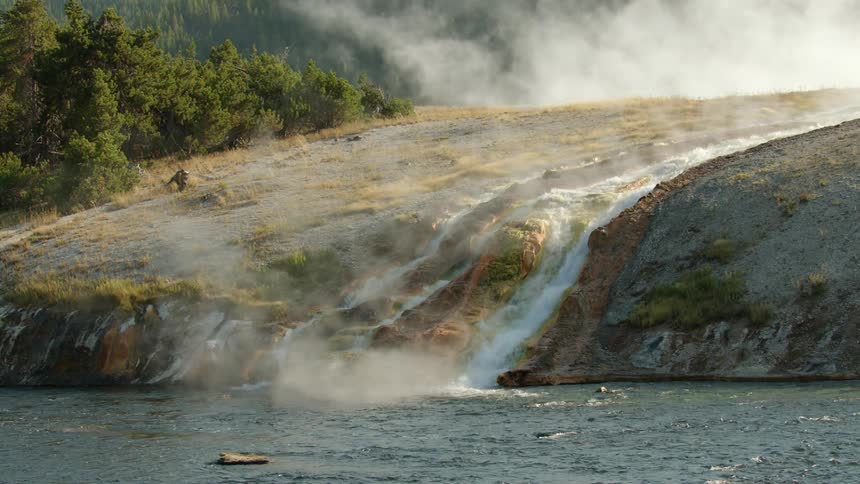 A geothermal hot spring cascades down a hillside into a river