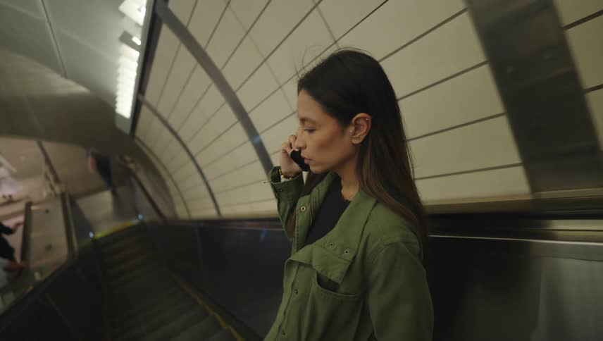 A woman is talking on her cell phone while riding the escalator