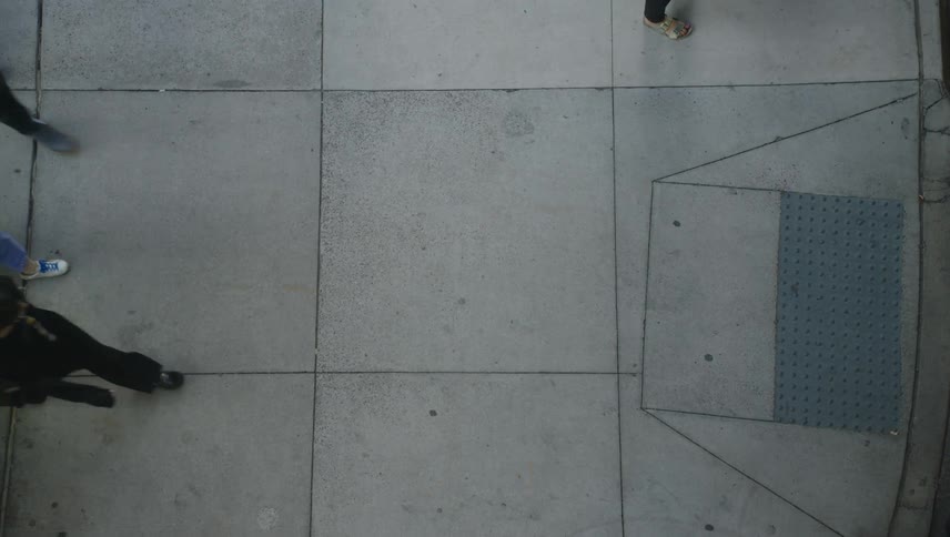 An overhead view of a sidewalk with people walking in different directions and queueing to enter a building