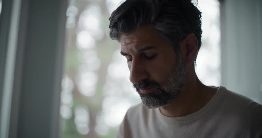 Bearded man wearing a cream sweatshirt looks out the window