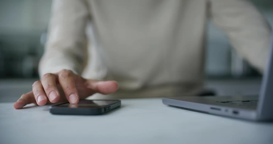 Persons hand typing on a laptop and interacting with a smartphone