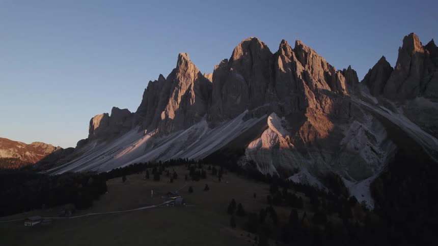 A mountain range with sharp rocky peaks illuminated by the setting sun casting long shadows across the valleys