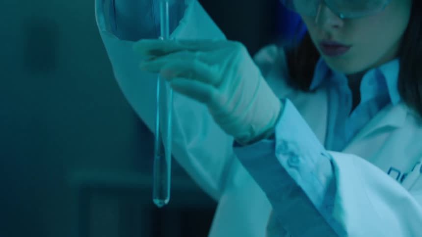 A laboratory technician illuminated by blue lights fills a test tube