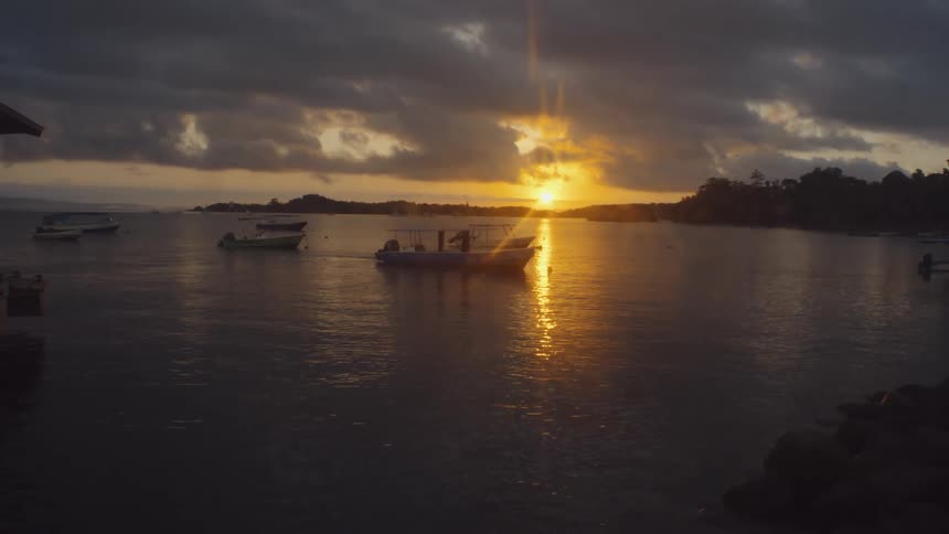 A large lake with some boats stopped and the sun reflecting on the surface of the water at dusk